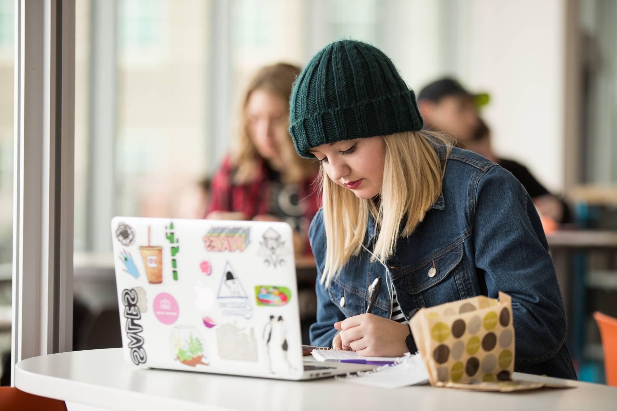 Student studying in the library with laptop and notebook